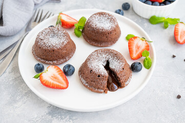 Chocolate fondant lava cake with fresh berries on a plate on a gray background.