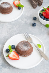 Chocolate fondant lava cake with fresh berries on a plate on a gray background.