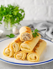 Pancakes or thin crepes stuffed with chicken and mushrooms on a plate on a gray concrete background. Selective focus, copy space.