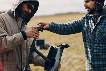 Two men pilots holding quadcopter drone in hands at outside field