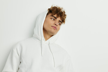 a cute man stands on a white background in a white hoodie with a hood on his head and looks pleasantly into the camera