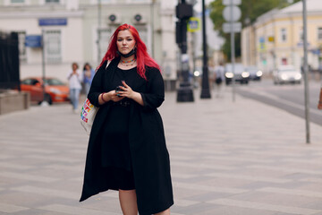 European plus size woman walking outdoor street city with mobile cellular phone. Young red pink haired body positive girl using cellphone smartphone