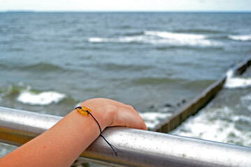 A child's hand on the railing of the embankment against the backdrop of the restless Baltic Sea. On the wrist is a bracelet with amber. Zelenogradsk, Kaliningrad region