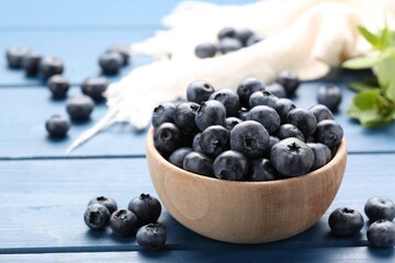 Tasty fresh blueberries and green leaves on blue wooden table, closeup
