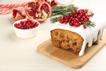 Traditional classic Christmas cake decorated with cranberries, pomegranate seeds and rosemary on white wooden table