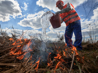 Fireman ecologist fighting fire in field with cloudy sky on background. Low angle view of male...