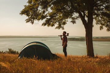 Male camper with axe standing near tent at lakeside during hiking trip