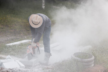 Worker mason cuts the sidewalk tile with circular saw while repairing sidewalk in city street.