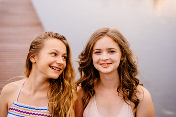 Summer portrait of two teeneger girl friends on wooden bridge at nature outdoors.