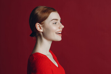 Portrait of young smile ginger woman profile portrait on red background.