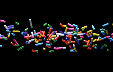 Small sprinkle colorful sugar candies flying sweet food. isolated on a black background