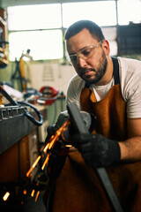 Fototapeta na wymiar A manual worker in a wheelchair is grinding metal bars in a workshop.