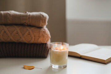 cozy comfortable home autumn still life with a candle, book, knitted sweaters and plaid