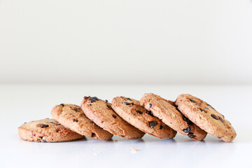 A line of six delicious chocolate chip cookies on a white table, tasty biscuit snack