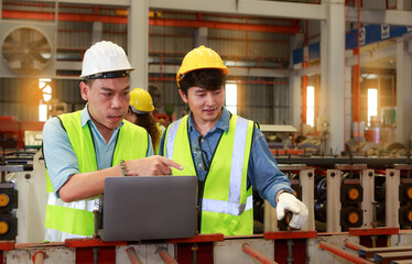 Asian male Hard Hat chief engineer using laptop to train workers to check checks heavy metal machinery