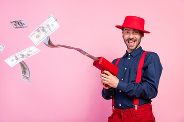 Photo of excited positive handsome guy use money gun flying bills isolated on pink color background