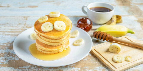 Stack of  banana pancakes with slices of fresh bananas, a Sweet Homemade Stack of Pancakes with Butter and Syrup for Breakfast in wooden background