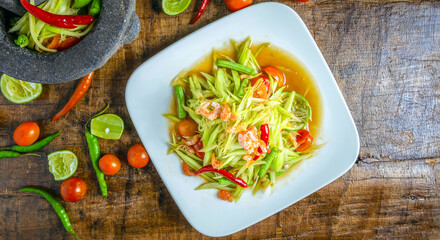 Thai food papaya salad on a plate with lemon and tomato on a wooden background.Top view