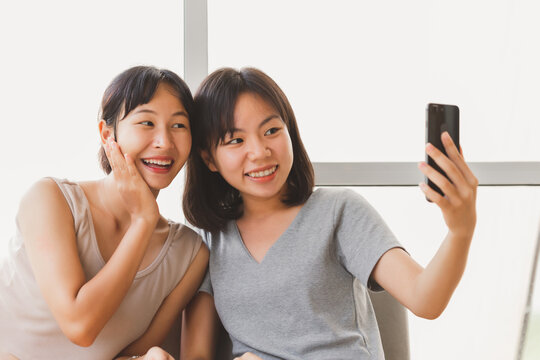Young happy attractive Asian teenager students taking selfie with friend indoor coffee cafe. Cheerful girl friends taking photos together with happy fun moment. LGBT lesbian couple life style concept.