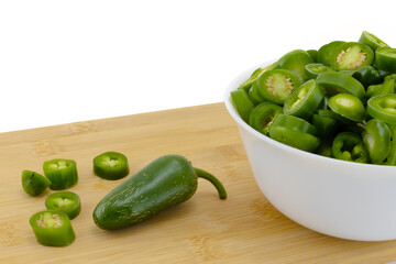 Still life with green unripe fresh sliced jalapeno pepper in white bowl on wooden board and white background. Organic chili pepper. Mexican cuisine concept ideas