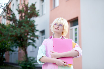student girl holding pink folder with books, looking up thoughtfully, walking in school campus, education concept - obrazy, fototapety, plakaty