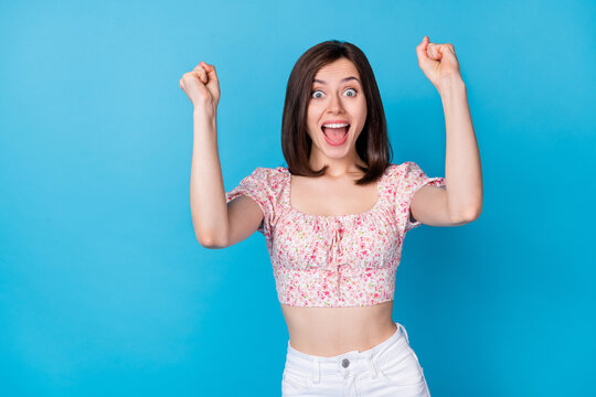 Portrait photo of young pretty girlish woman wear cropped shirt fists up celebrate victory isolated on blue color background