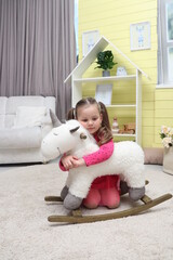 Little girl with a unicorn in the children's room. Child 4-5 years old in a children's room with toys. A baby in a pink dress is sitting on the floor near a white pony. The child plays alone in the