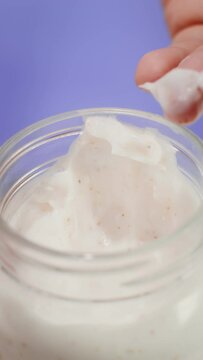 A woman picks up a cream from a transparent jar with her fingers. Close-up of a hand, vertical video