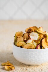 Dried sliced apples in a brown bowl on a light concrete background. Natural fruit chips. Healthy food.Dried sliced apples in a brown bowl on a light concrete background. Natural fruit chips.