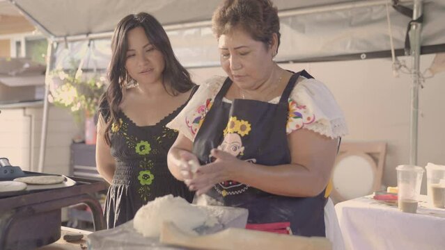 Indigenous daughter asking her mother how to do something while she cooks and nods yes.