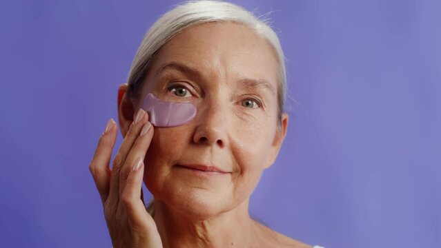 Elderly model with patches on eyelid posing while looking at camera while standing against studio background