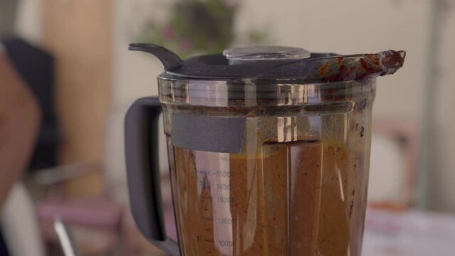 Closeup of a blender blending while an Indigenous woman does things in the background. 