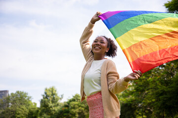 Portrait of young lesbian woman waving pride rainbow flag in their backs supporting LGBTQ pride in the park. Independence and gender diversity. Supporters of the LGBT community 