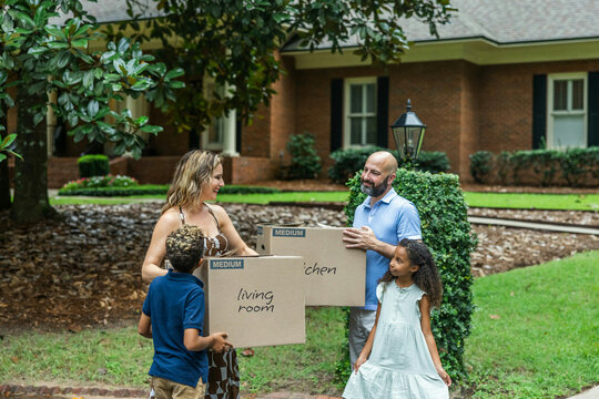 A blended family mom and dad and two young children holding packing boxes and moving into their new home