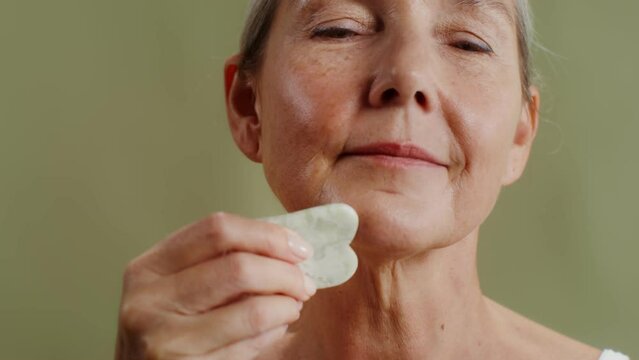Elderly woman makes face massage with gua sha stone