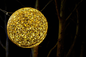 Close up of an illuminated Christmas ball at night. Round sphere in gold color.