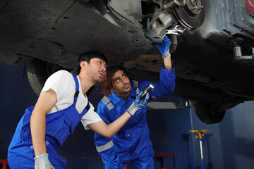 Male car operator wearing blue overalls,cap and gloves working under the hood of white car and checking attentively serviceability of engine at repair garage. Concept of car maintenance