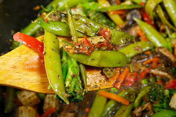 Stewed vegetables broccoli tomatoes and green peas with a wooden spoon close-up.
