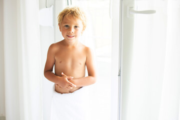 Cute blond toddler child with white tower around belly, sitting in bed with glass of water after bath