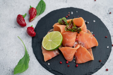 Fresh salmon slices with peppers, greens and lime on concrete background