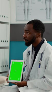 Vertical video: Doctor using greenscreen dispay on digital tablet at checkup visit with pregnant woman. Health specialist showing mockup template with isolated chroma ley and blank copyspace to