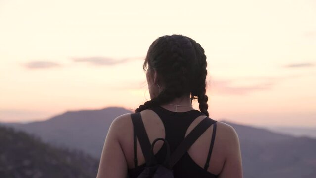 Young Native American woman's back as she looks off into the distance of a sunset over a mountain.