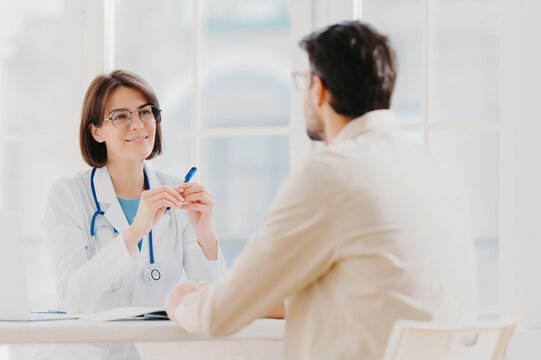 Heath Care And Medical Consultancy Concept. Skilled Therapist In White Uniform Talks With Patient, Writes Down In Medical History, Listens Attentively All Symptoms, Tries To Prevent Serious Disease