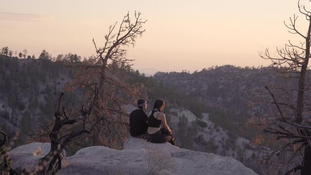 Young Native American hikers sitting on a boulder to watch the sun set on a mountain peak.