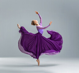 Ballerina in purple ballet leotard and violet long ballet skirt dancing in white studio on pointe shoes. - obrazy, fototapety, plakaty