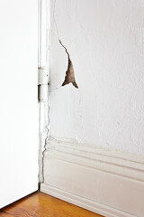 Damaged property: white wall behind a door hinge with a crack or rip and a piece of plaster missing. Cheap construction material concept.
