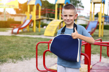 Fototapeta na wymiar happy child with broken limb arm outdoors on playground background. school boy had accident on summer vacation. kid in a cast on hand. concept of health and medical.