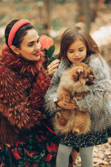Mom and daughter walking the dog outside, fashion people in jackets and black dresses with a pomeranian dog