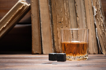  Whiskey in the drinking glass and old books on the brown wooden table background. Front view.