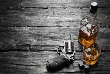 Glass of whiskey and black gun on the wooden table background.